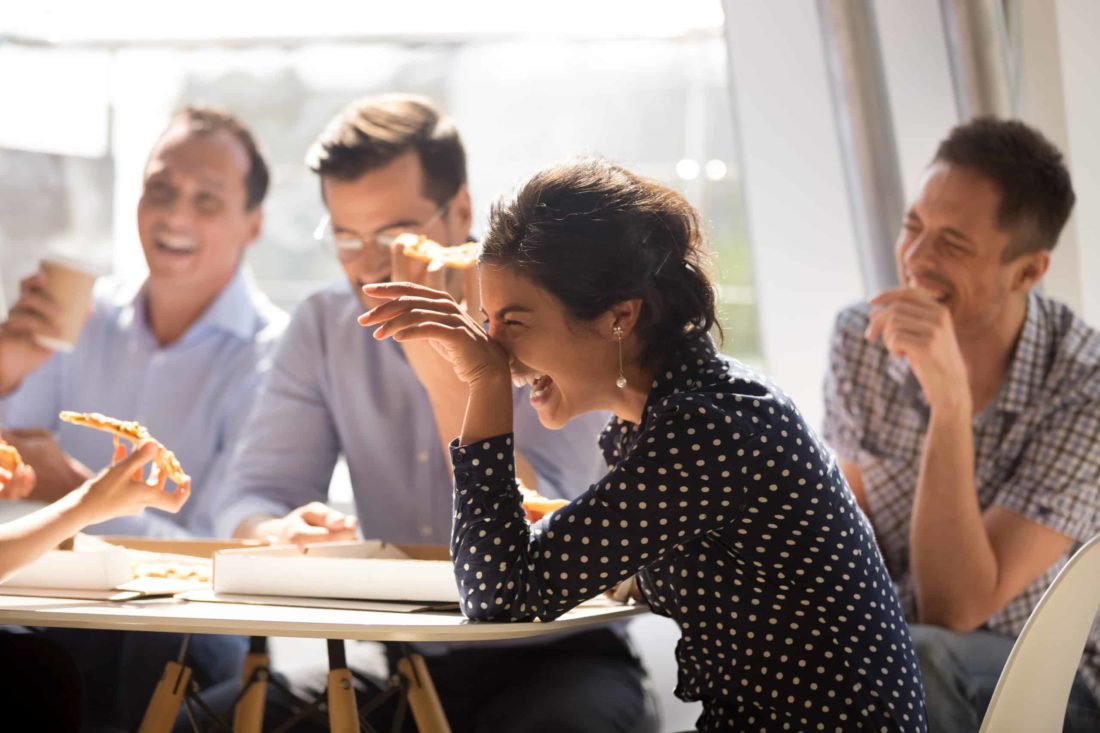 Business lady laughs during lunch with her coworkers while they eat pizza
