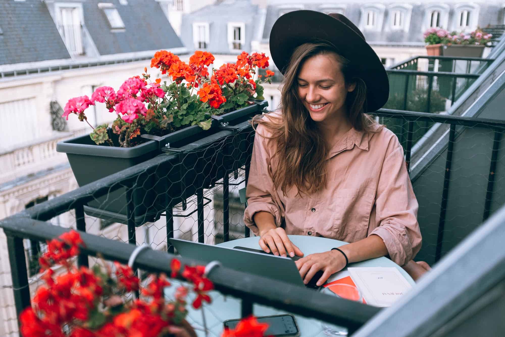 Girl sits on decorated balcony and types on her keyboard on her laptop about Key Components Businesses Need to Succeed in Remote Work